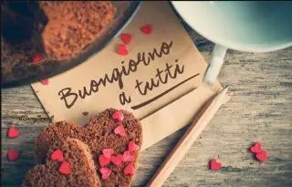 tavolo con sopra una tazza dei biscotti a forma di cuore e un biglietto con su scritto buongiorno a tutti