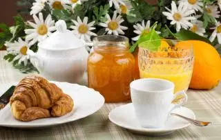 tavolo con tovaglia con sopra dei fiori e una colazione con cornetto caffè marmellata e spremuta d'arancia